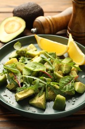Photo of Tasty cut avocados with arugula, lemon and dressing on wooden table, closeup