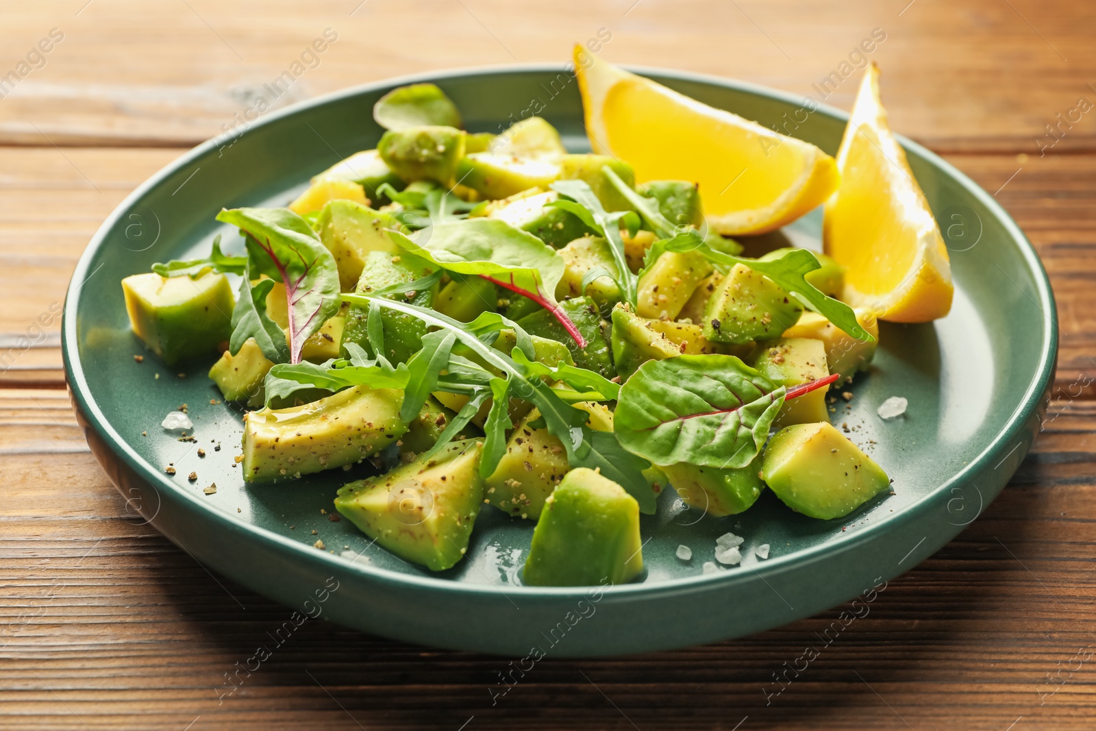 Tasty cut avocados with arugula, lemon and dressing on wooden table, closeup Photo of Tasty cut avocados with arugula, lemon and dressing on wooden table, closeup