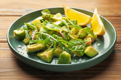 Photo of Tasty cut avocados with arugula, lemon and dressing on wooden table, closeup