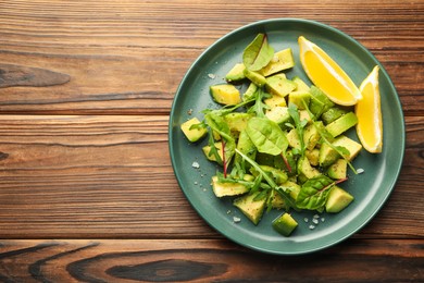 Photo of Tasty cut avocados with arugula, lemon and dressing on wooden table, top view. Space for text