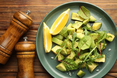 Photo of Tasty cut avocados with arugula, lemon and dressing on wooden table, flat lay
