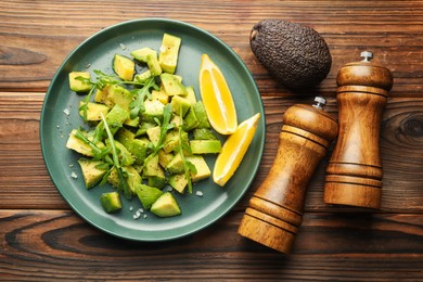 Photo of Tasty cut avocados with arugula, lemon and dressing on wooden table, flat lay
