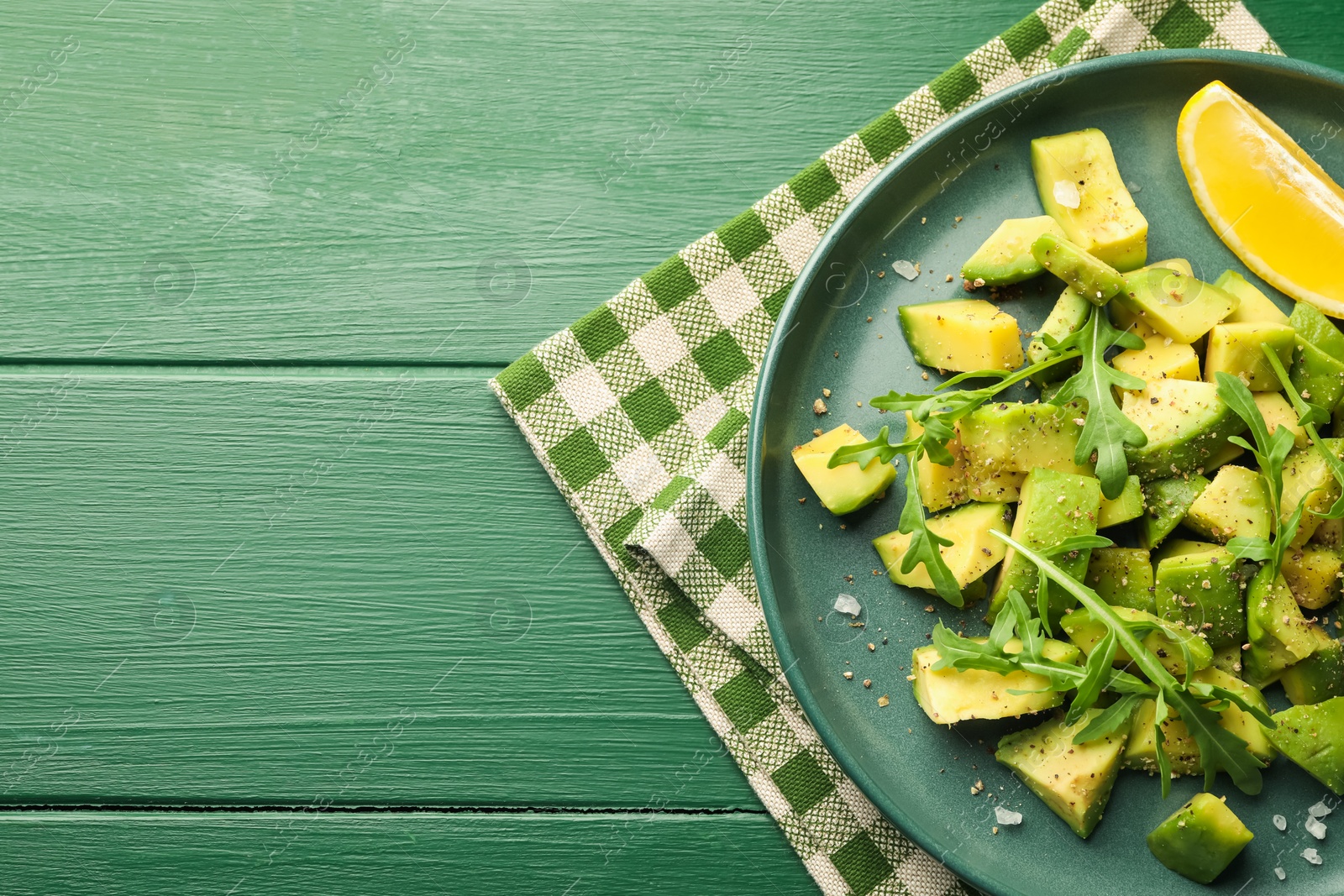 Tasty cut avocados with arugula, lemon and dressing on green wooden table, top view. Space for text Photo of Tasty cut avocados with arugula, lemon and dressing on green wooden table, top view. Space for text
