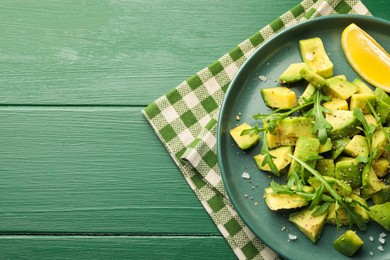 Photo of Tasty cut avocados with arugula, lemon and dressing on green wooden table, top view. Space for text