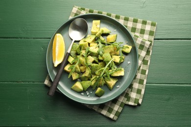 Photo of Tasty cut avocados with arugula, lemon and dressing on green wooden table, top view