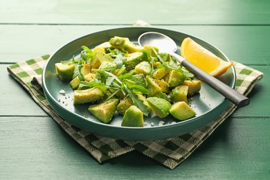 Photo of Tasty cut avocados with arugula, lemon and dressing on green wooden table, closeup