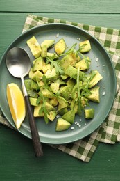 Photo of Tasty cut avocados with arugula, lemon and dressing on green wooden table, top view