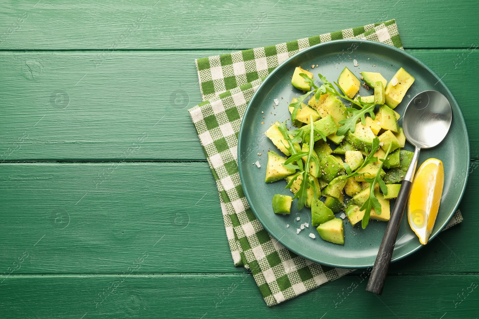 Tasty cut avocados with arugula, lemon and dressing on green wooden table, top view. Space for text Photo of Tasty cut avocados with arugula, lemon and dressing on green wooden table, top view. Space for text