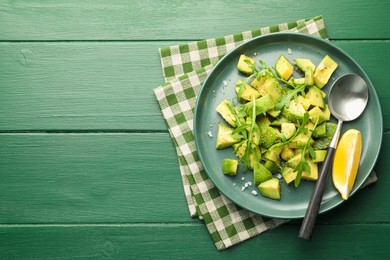 Photo of Tasty cut avocados with arugula, lemon and dressing on green wooden table, top view. Space for text