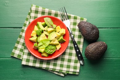 Photo of Tasty cut avocados with spinach and dressing on green wooden table, flat lay