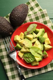 Photo of Tasty cut avocados with spinach and dressing on green wooden table, flat lay