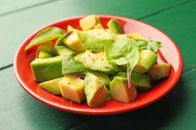 Photo of Tasty cut avocados with spinach and dressing on green wooden table, closeup
