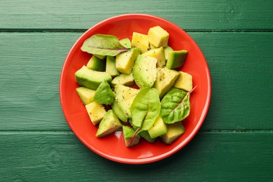 Photo of Tasty cut avocados with spinach and dressing on green wooden table, top view