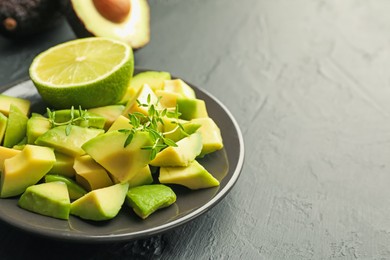 Photo of Tasty cut avocados, thyme and lime on black table, closeup. Space for text