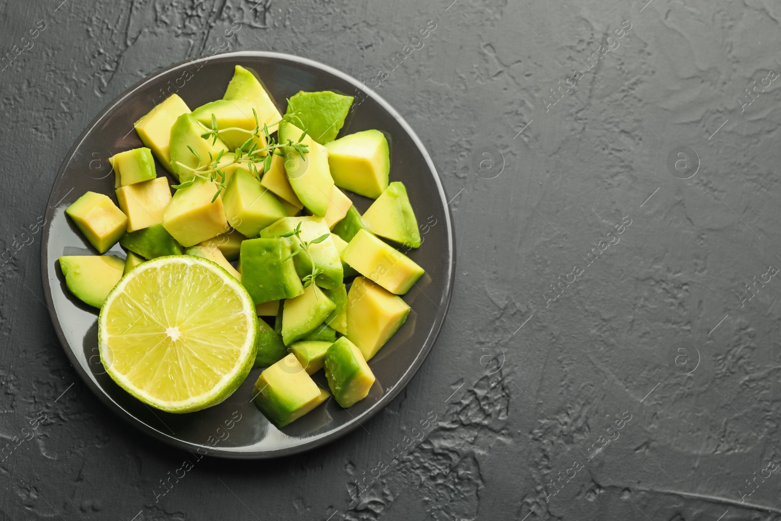 Tasty cut avocados, thyme and lime on black table, top view. Space for text Photo of Tasty cut avocados, thyme and lime on black table, top view. Space for text