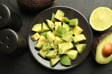 Photo of Tasty cut avocados, thyme and lime on black table, flat lay