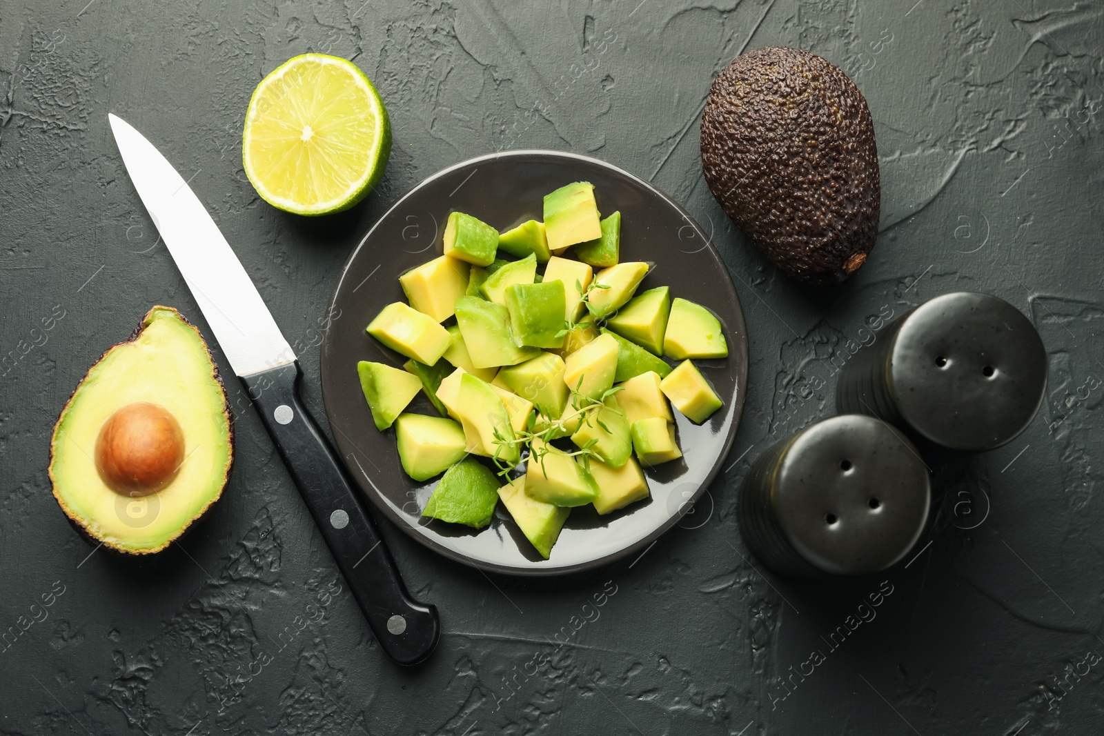 Tasty cut avocados, thyme, knife and lime on black table, flat lay Photo of Tasty cut avocados, thyme, knife and lime on black table, flat lay