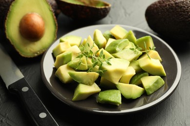Photo of Tasty cut avocados, thyme and knife on black table, closeup