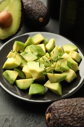 Photo of Tasty cut avocados and thyme on black table, closeup