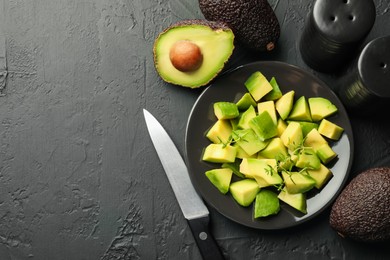 Photo of Tasty cut avocados, thyme and knife on black table, flat lay. Space for text