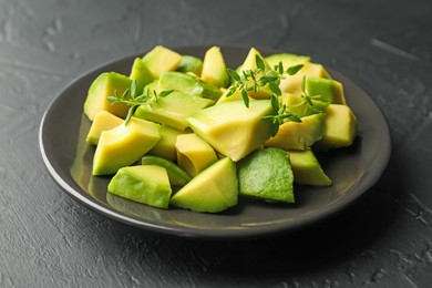 Photo of Tasty cut avocados and thyme on black table, closeup