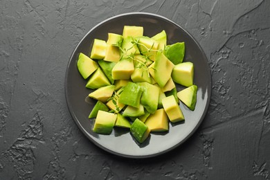 Photo of Tasty cut avocados and thyme on black table, top view