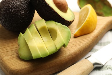 Photo of Tasty cut avocados, lemon and knife on table, closeup