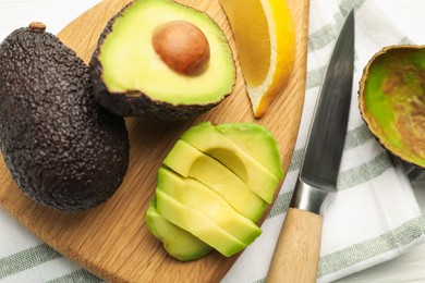 Photo of Tasty cut avocados, lemon and knife on white wooden table, flat lay