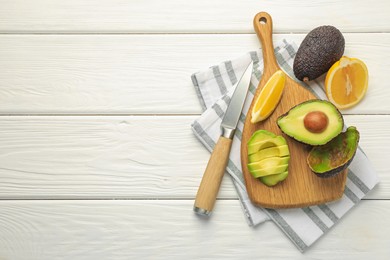 Photo of Tasty cut avocados, lemon and knife on white wooden table, flat lay. Space for text
