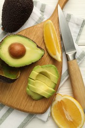 Photo of Tasty cut avocados, lemon and knife on white wooden table, flat lay