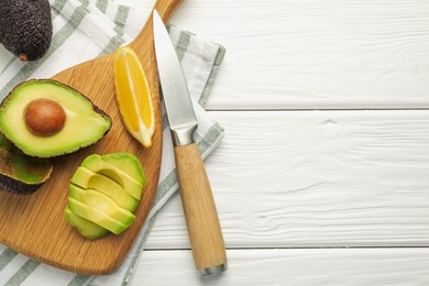 Photo of Tasty cut avocados, lemon and knife on white wooden table, flat lay. Space for text