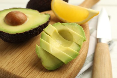 Photo of Tasty cut avocados, lemon and knife on white wooden table, closeup