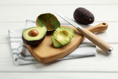 Photo of Tasty cut avocados and knife on white wooden table