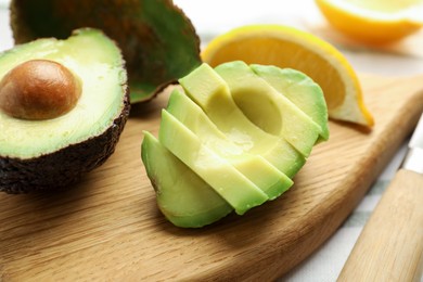 Photo of Tasty cut avocados, lemon and knife on table, closeup