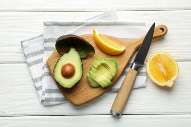 Photo of Tasty cut avocados, lemon and knife on white wooden table, flat lay