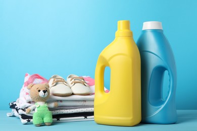 Photo of Bottles of fabric softener, stacked baby clothes, shoes and toy on light blue background