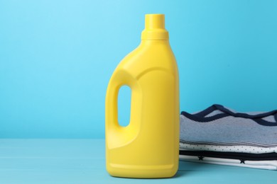 Photo of Bottle of fabric softener and stacked baby clothes on light blue background
