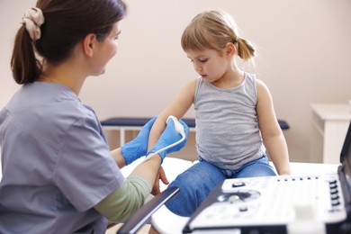 Photo of Sonographer conducting ultrasound examination of little girl's arm in clinic