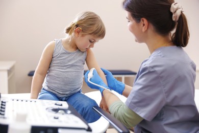 Photo of Sonographer conducting ultrasound examination of little girl's arm in clinic