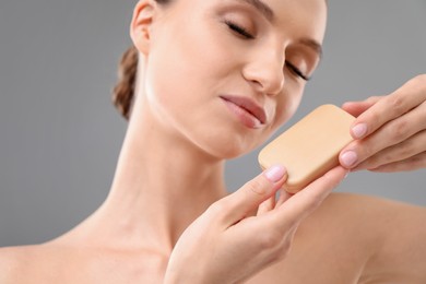 Photo of Beautiful woman with soap bar on grey background, closeup