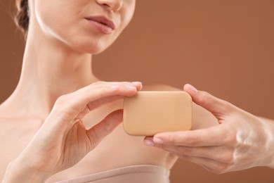 Photo of Woman with soap bar on brown background, closeup