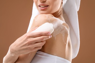 Photo of Smiling woman washing body with soap bar on brown background, closeup