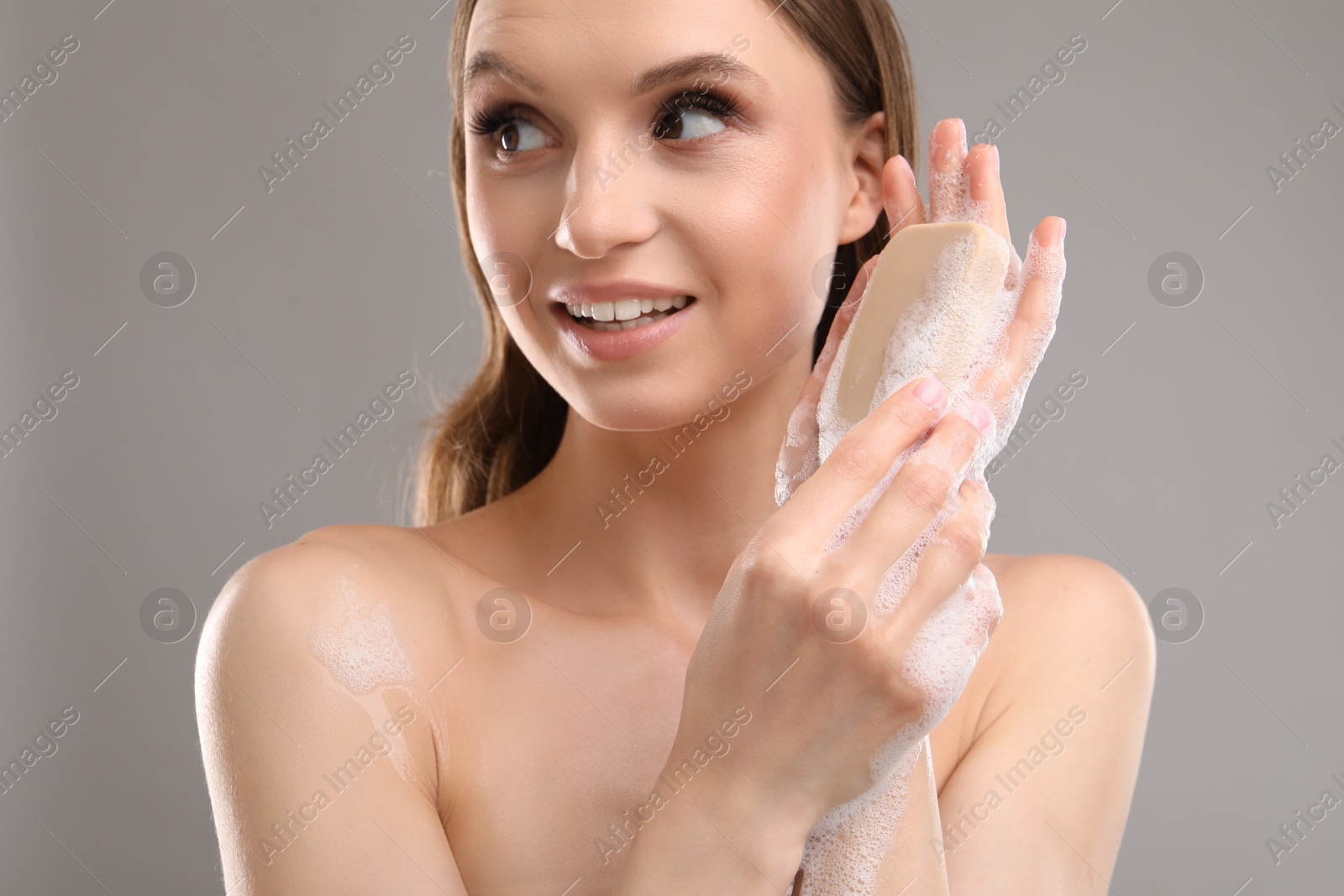 Smiling woman with soap bar on grey background, closeup Photo of Smiling woman with soap bar on grey background, closeup