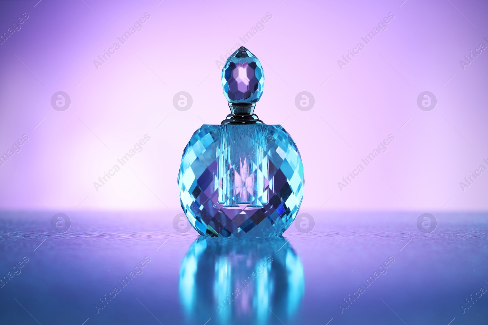 Bottle of perfume on mirror surface against violet gradient background Photo of Bottle of perfume on mirror surface against violet gradient background