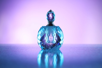 Photo of Bottle of perfume on mirror surface against violet gradient background