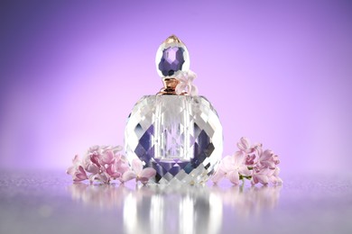 Photo of Beautiful lilac flowers and perfume on mirror surface against violet gradient background