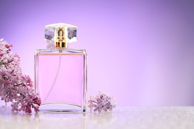 Photo of Beautiful lilac flowers and perfume on mirror surface against violet gradient background, space for text