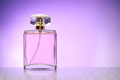 Photo of Bottle of perfume on mirror surface against violet gradient background, space for text