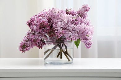 Photo of Beautiful lilac flowers in glass vase on white table indoors