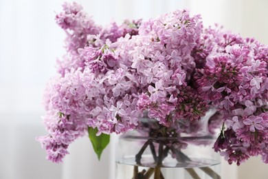 Photo of Beautiful lilac flowers in glass vase indoors, closeup